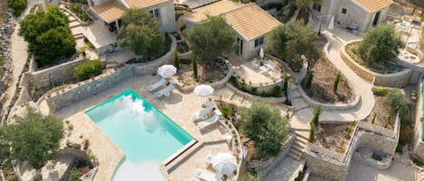 Oversigtsbillede af et resort med flere stenhuse, en central pool og udendørs siddepladser.