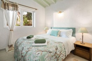 Un dormitorio con cama, dos lámparas de noche, una ventana con cortinas y una mesita de noche.