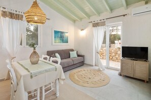 Ein Wohnzimmer mit Esstisch, Sofa, TV-Schrank und großem Fenster.