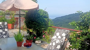 An outdoor dining area with a table, chairs, and an umbrella. There are potted plants and a view of a mountainous landscape. - Anastasia's Cottage in Pelion (Makrirrachi)