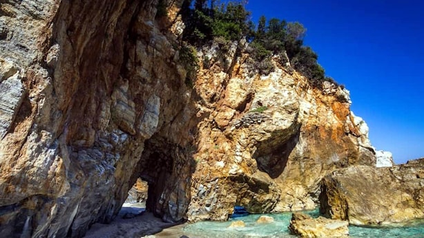 A rocky coastal landscape with clear turquoise waters and a large rock formation. - Anastasia's Cottage in Pelion (Makrirrachi)