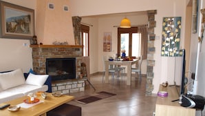 A living room with a fireplace, a dining area, and a kitchen. - Anastasia's Cottage in Pelion (Makrirrachi)