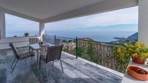 Un balcón con mesa y sillas, vista al mar y barandilla.