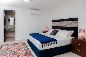 A neatly arranged bedroom with a bed, bedside table, and a nightstand. - Mojarra: Suite, Design with Kitchenette and Sofa Bed (Cancún)
