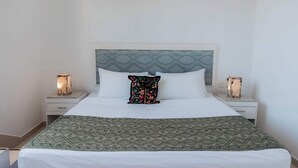 A neatly made bed with a patterned bedspread, a decorative pillow, and two bedside lamps on white nightstands. - Mojarra: Tropical Suites Downtown Cancún (Cancún)