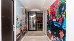 A hallway with a glass door leading to a dining area, a large colorful mural on the right wall, and a modern interior design. - Mojarra: Tropical Suites Downtown Cancún (Cancún)