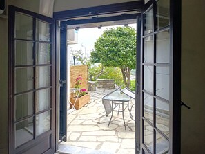 An open door leading to a patio with a table and chairs, a potted plant, and a stone wall. - Villa Zina  Studio 2 (Agios Dimitrios Piliou)