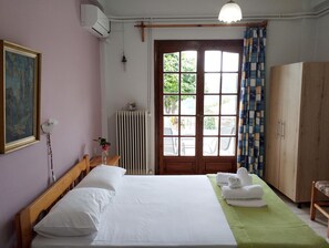 Un dormitorio con cama, radiador, ventana con cortinas, armario de madera y un cuadro en la pared.