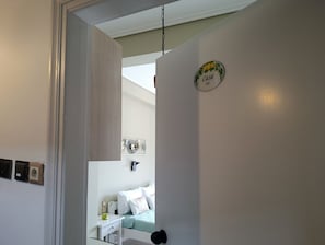A hallway with a bed, a bedside table, and a wall-mounted light fixture. - Villa Zina  Studio 2 (Agios Dimitrios Piliou)