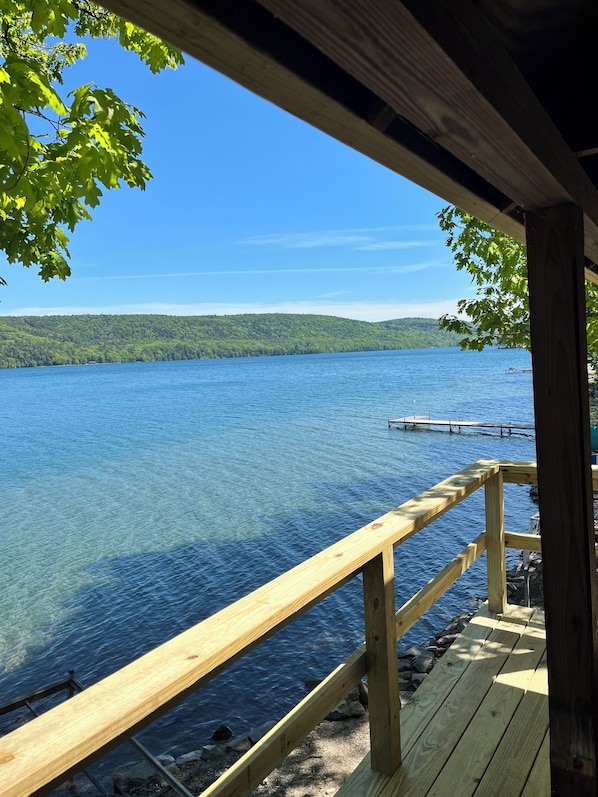 A wooden deck overlooking a clear lake with a dock and forested hills in the background.