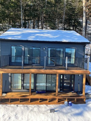 A two-story house with a balcony, large windows, and a snow-covered roof.
