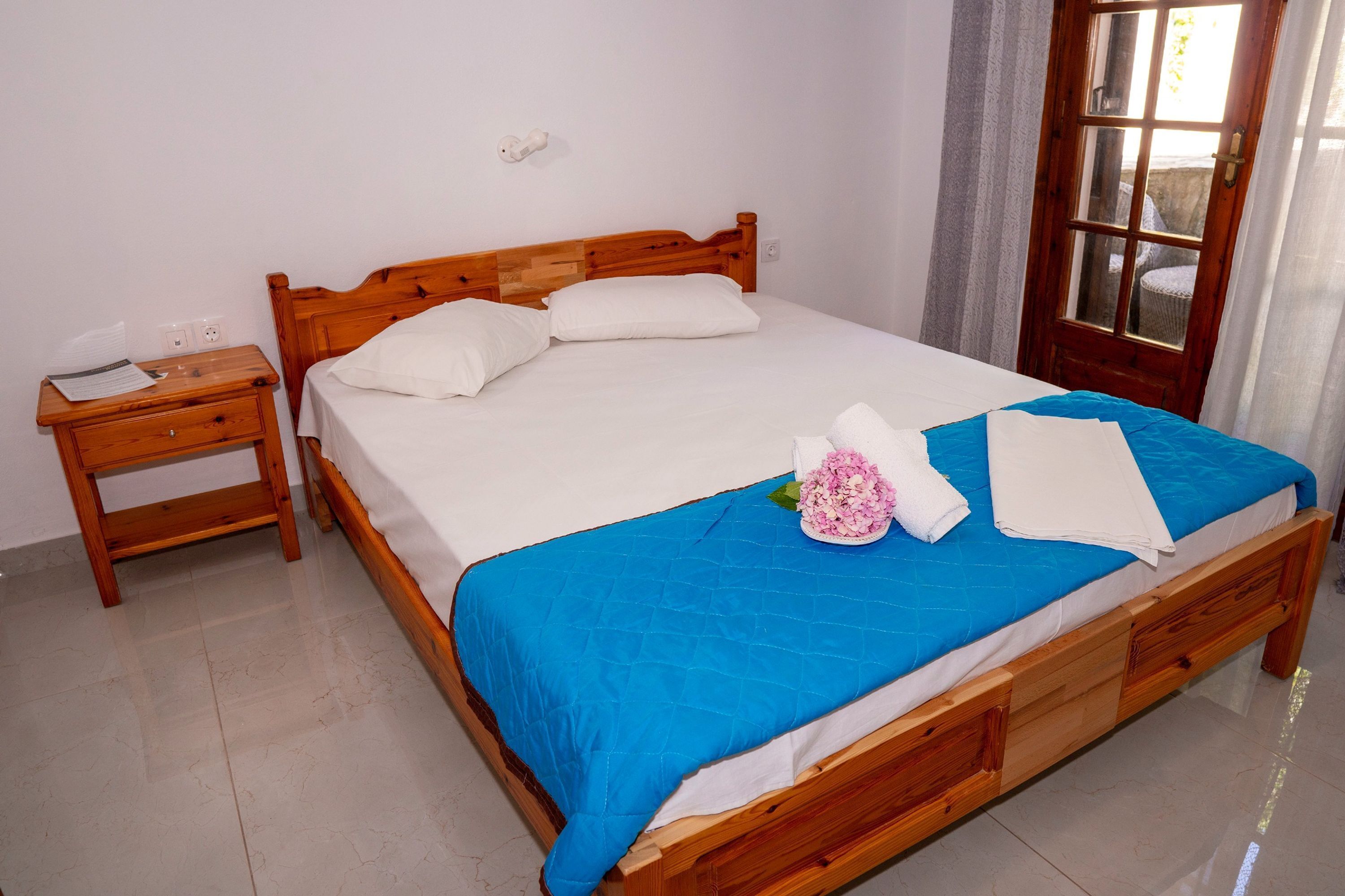 Una cama bien hecha con una colcha azul, almohadas blancas y un arreglo floral.
