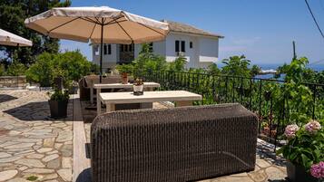 Eine Terrasse im Freien mit Korbmöbeln, einem Tisch und einem großen Sonnenschirm.