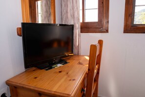 A wooden TV stand with a flat-screen TV, positioned in a corner with windows and curtains. - Paradeisos Double Room with Sea View (4) (Agios Dimitrios Piliou)