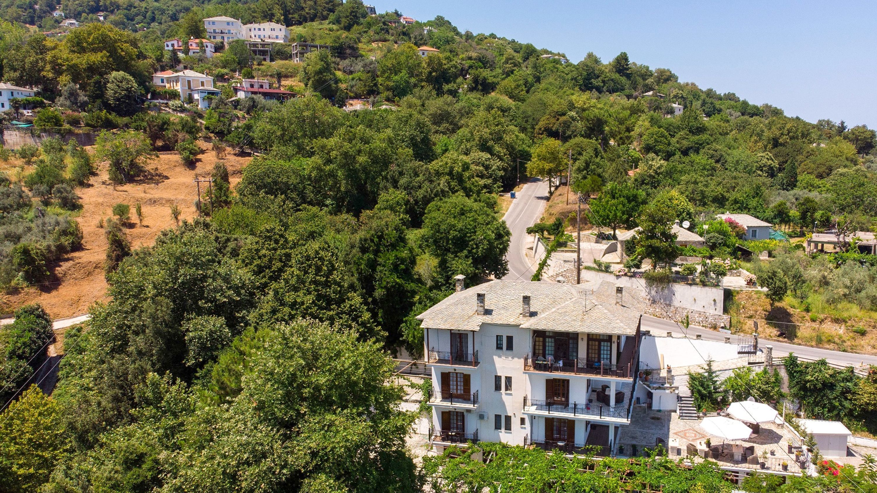 Un edificio a più piani con un balcone, immerso nel verde e circondato da un pendio.