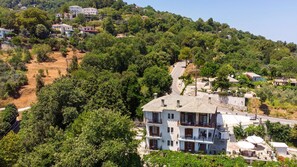 Un edificio a più piani con un balcone, immerso nel verde e circondato da un pendio.