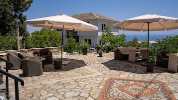 Area patio esterna con pavimento in pietra, mobili in vimini e ombrelloni color beige.