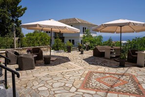 Eine Terrassenanlage im Freien mit Steinböden, Korbmöbeln und beigen Sonnenschirmen.
