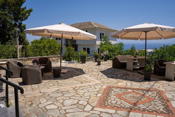Area patio esterna con pavimento in pietra, mobili in vimini e ombrelloni color beige.