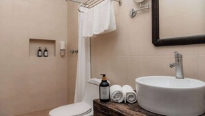 A bathroom with a toilet, a sink, a towel rack, a shower curtain, and a bottle of body wash. - Mojarra: Suites with Balcony in Cancún Heart (Cancún)