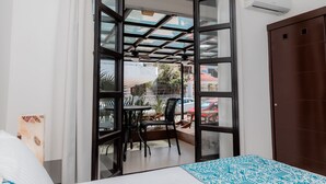 A room with a bed, a window with a view of the street, a table with chairs, and a brown door. - Mojarra: Suites with Balcony in Cancún Heart (Cancún)