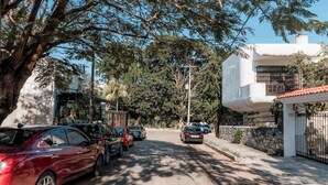 A street view with parked cars, a white building with a red roof, and trees providing shade. - Mojarra: Suites with Balcony in Cancún Heart (Cancún)