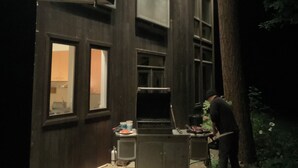 Ein modernes Gebäude mit dunklen Hollfassaden, mehreren Fenstern und einem Baum im Vordergrund.