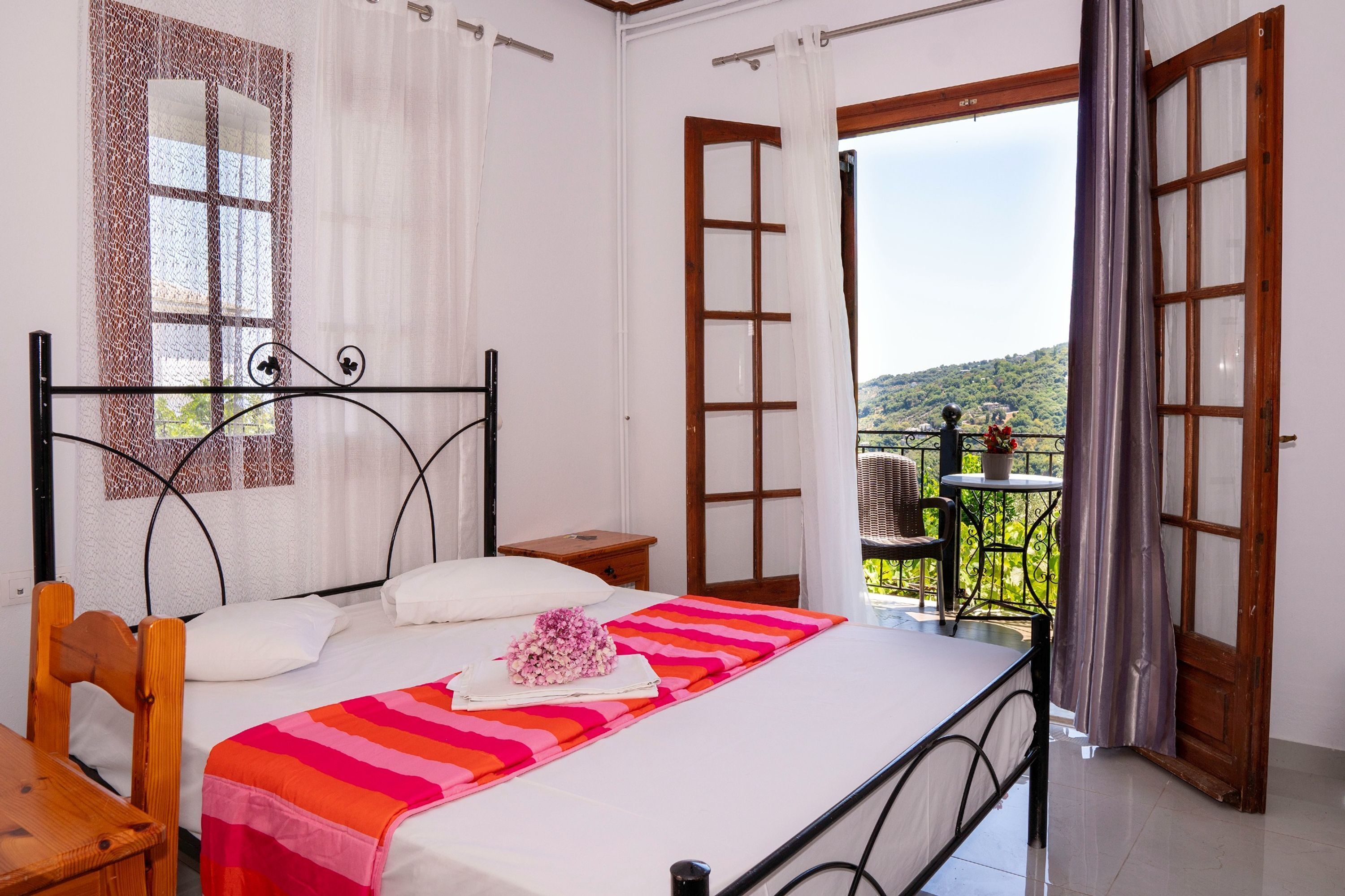 Una camera da letto con un letto, una sedia, un tavolino e un balcone vista campagna.