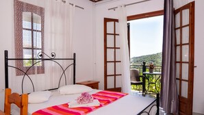 Un dormitori amb un llit, una cadira, una taula petita, i un balcó amb vista al camp.