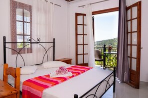 Una camera da letto con un letto, una sedia, un tavolino e un balcone vista campagna.