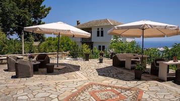 Zona patio con pavimento in pietra, mobili da esterno e ombrelloni, con vista su una casa e del verde.