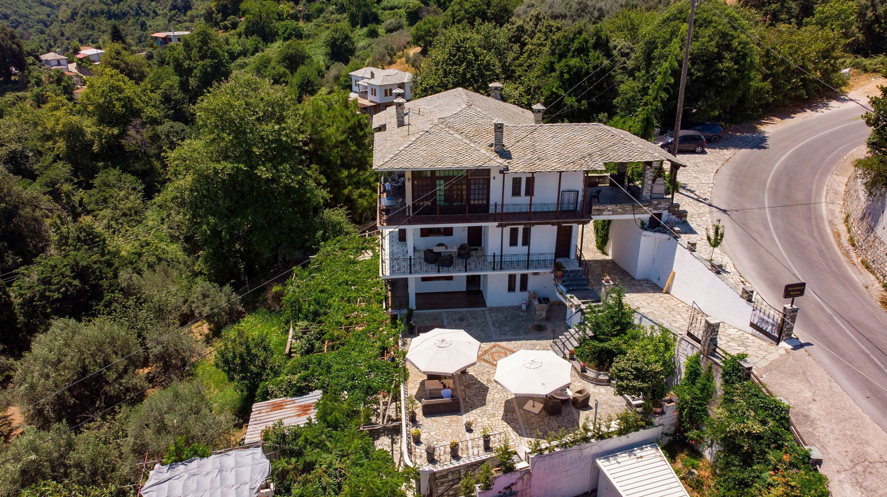 Una casa a due piani con un balcone, un patio in pietra e una strada curva nelle vicinanze.