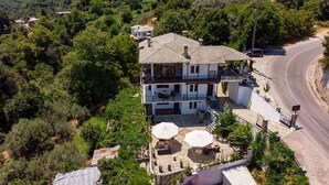 Una casa de dues plantes amb un balcó, un pati de pedra i un camí corbat a prop.