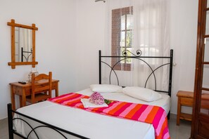 A neatly arranged bedroom with a bed, bedside table, chair, and a mirror on the wall. - Paradeisos Double Room with Balcony (2) (Agios Dimitrios Piliou)