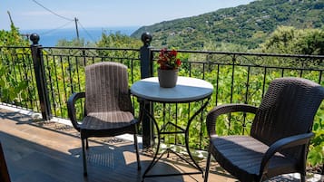 Un balcone con sedie in vimini e un tavolo, con vista su un paesaggio verdeggiante e il mare.