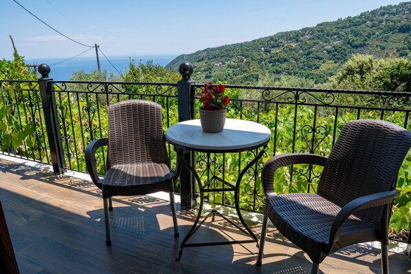 Un balcone con sedie in vimini e un tavolo, con vista su un paesaggio verdeggiante e il mare.