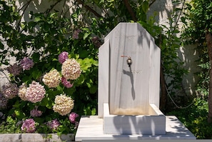 A gravestone with an inscription and a pipe, surrounded by hydrangea flowers. - Paradeisos Double Room with Balcony (2) (Agios Dimitrios Piliou)