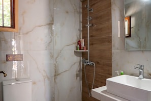 A bathroom with a white marble wall, a wooden panel wall, a white sink, and a shower with a handheld showerhead. - Paradeisos Double Room with Balcony (2) (Agios Dimitrios Piliou)