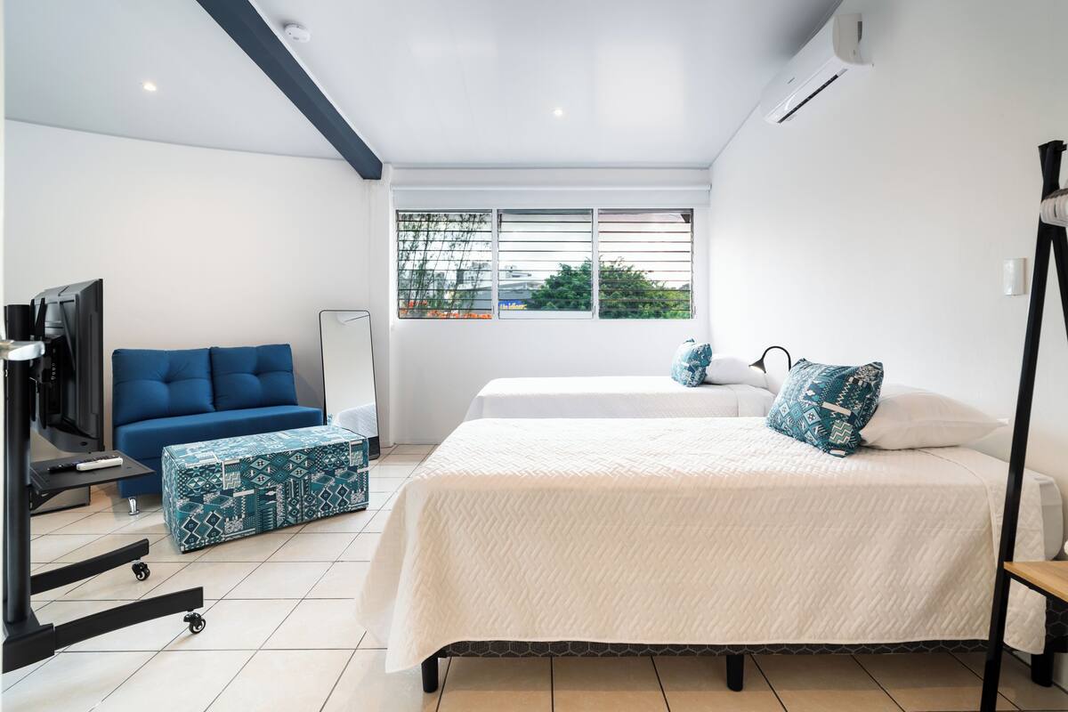 Een moderne slaapkamer met een bed, een bank, een televisie en een raam met zonwering.