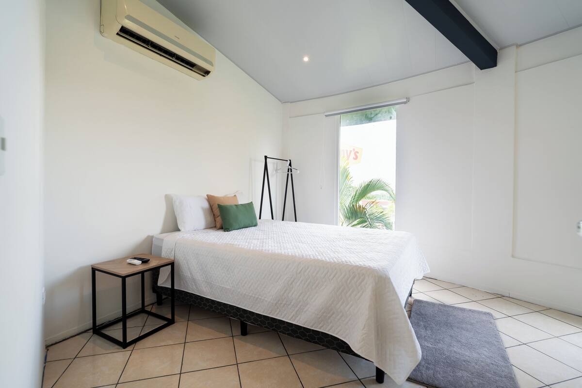Een slaapkamer met een bed, nachtkastje en een staande lamp.