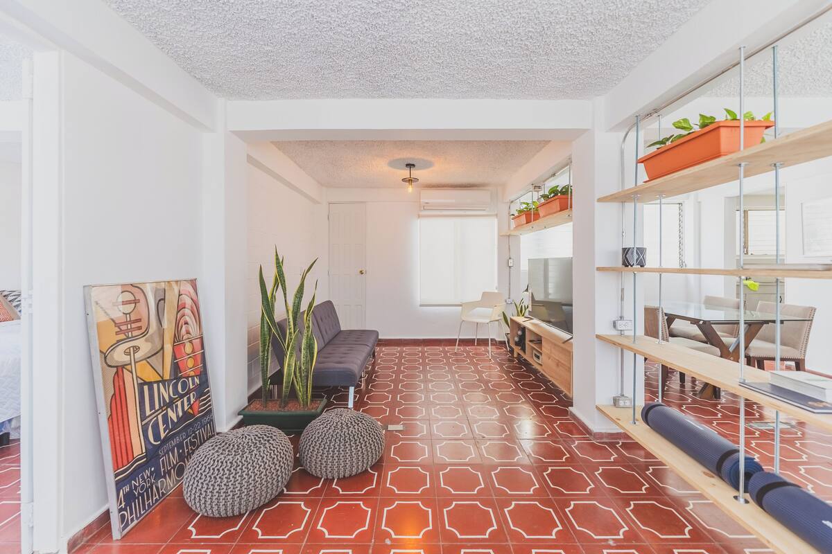 Een modern interieur met een vloer met een geometrisch patroon, een bank, een eethoek en planken met planten.