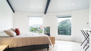 Een slaapkamer met een groot bed, een televisie en een stadsgezicht door grote ramen.