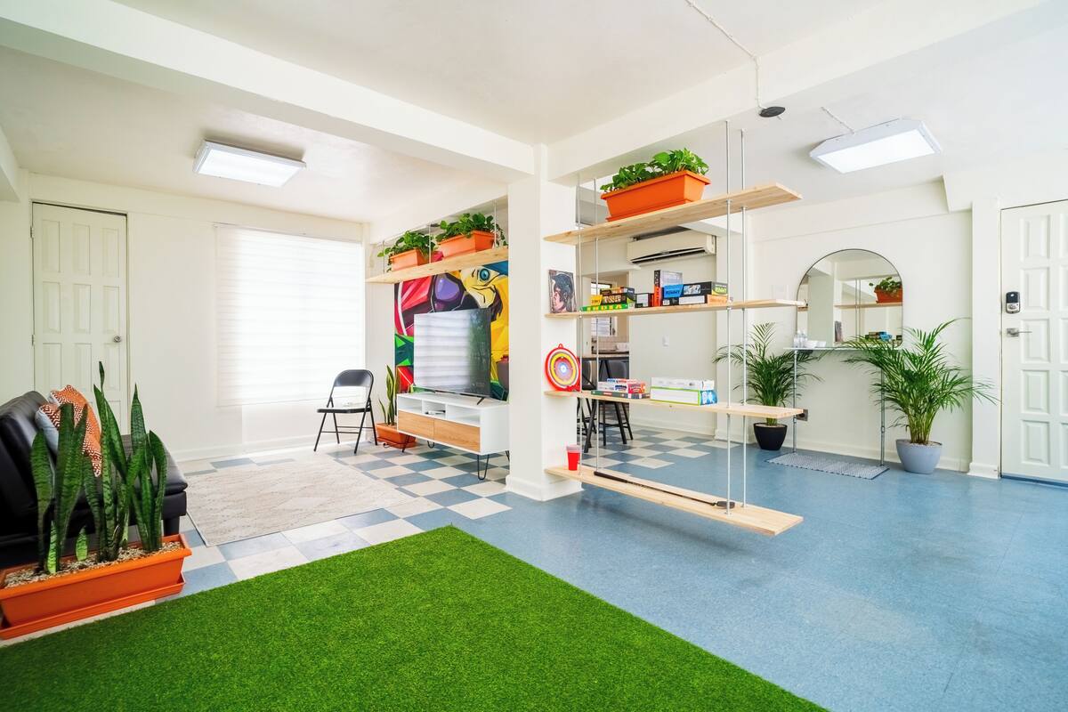 Een kamer met een zwart-wit betegelde vloer, een bureau met planken, een stoel, een bank en potplanten.
