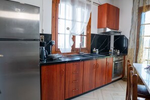 A kitchen with wooden cabinets, a stainless steel refrigerator, a black countertop, and a window with curtains. - Paradeisos Αpartment with Sea View (Agios Dimitrios Piliou)