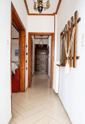 A hallway with wooden doors, a chandelier, and a coat rack with hanging items. - Paradeisos Αpartment with Sea View (Agios Dimitrios Piliou)