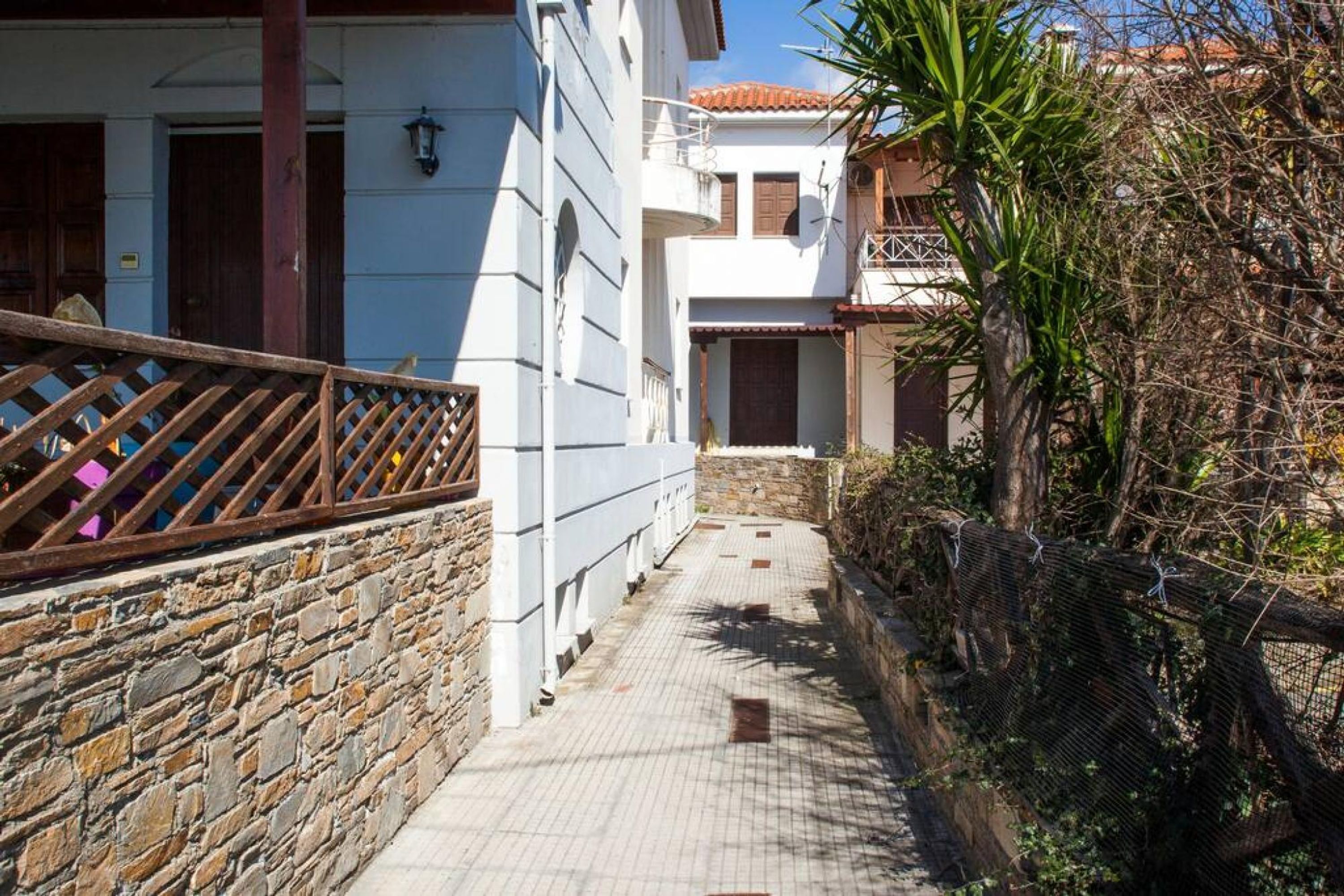 Uma passagem estreita com paredes de pedra, cerca de madeira e um edifício com telhado de cerâmica.