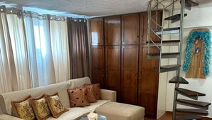 Una sala de estar con sofá, una mesa de centro, cama con toallas, una silla y una escalera.