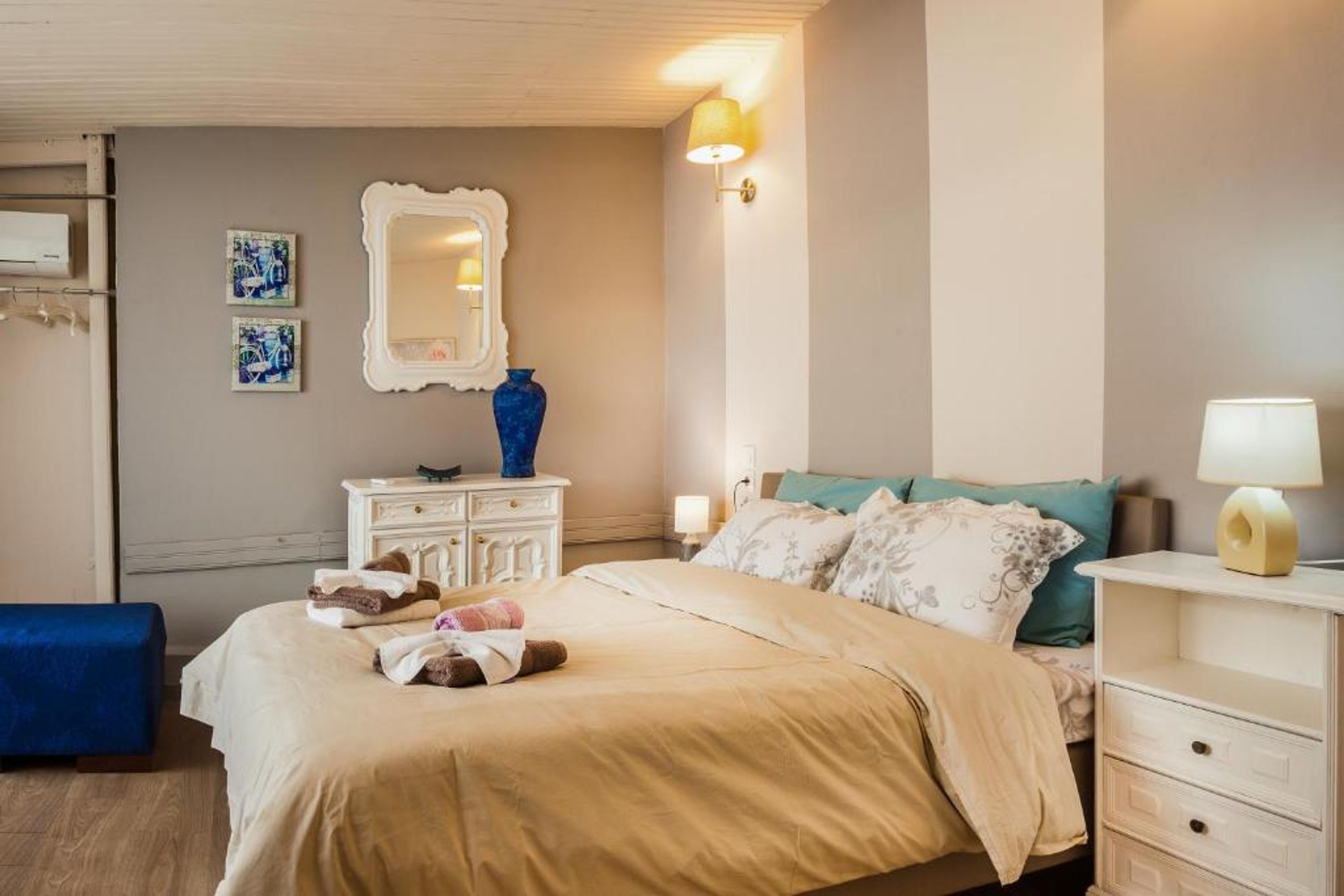 Une chambre à coucher comprenant un lit, des tables de chevet, un miroir et des œuvres d’art murales.
