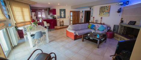 A spacious living area with a sofa, coffee table, and chairs. There is a dining area with a table and chairs. The room has a tiled floor and a fireplace.