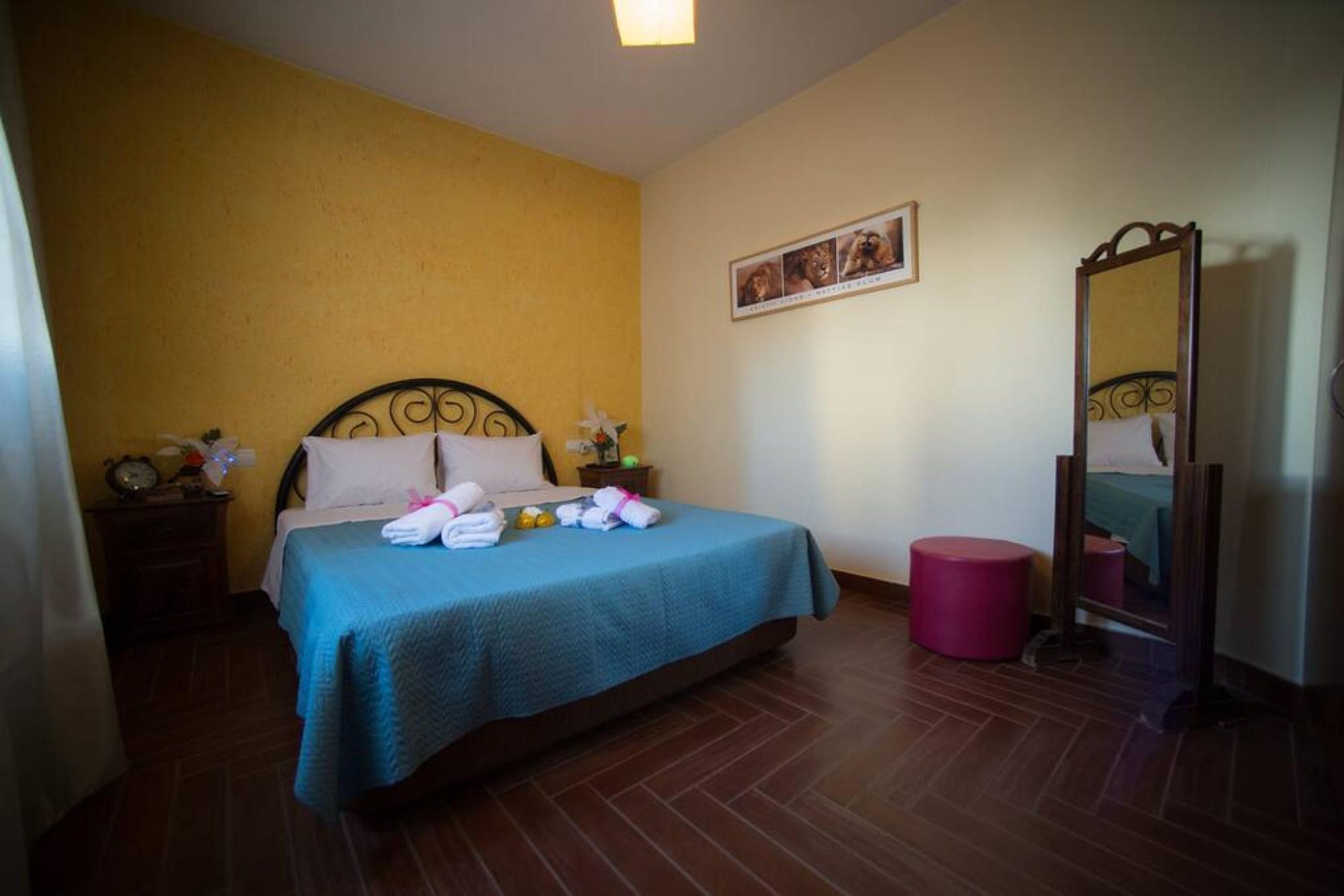 A hotel room with a bed, a bedside table, a mirror, and a wall-mounted picture.